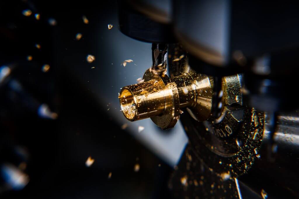 Swiss-type CNC lathe cutting brass component with chips flying from guide bushing